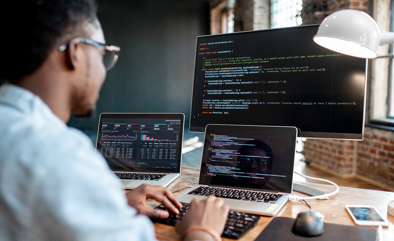 Male programmer coding with three monitors Male programmer coding with three monitors