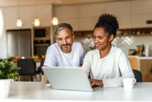 a man and a woman working on their computer in the kitchen