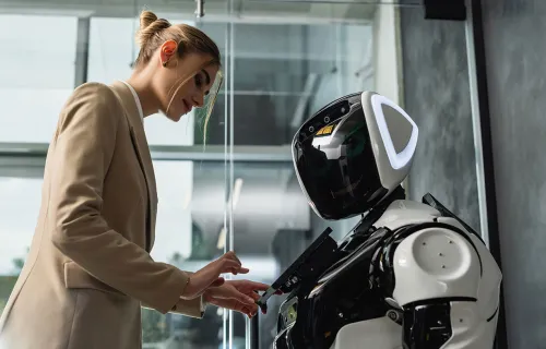 Woman in blazer interacts with humanoid robot in an office setting.